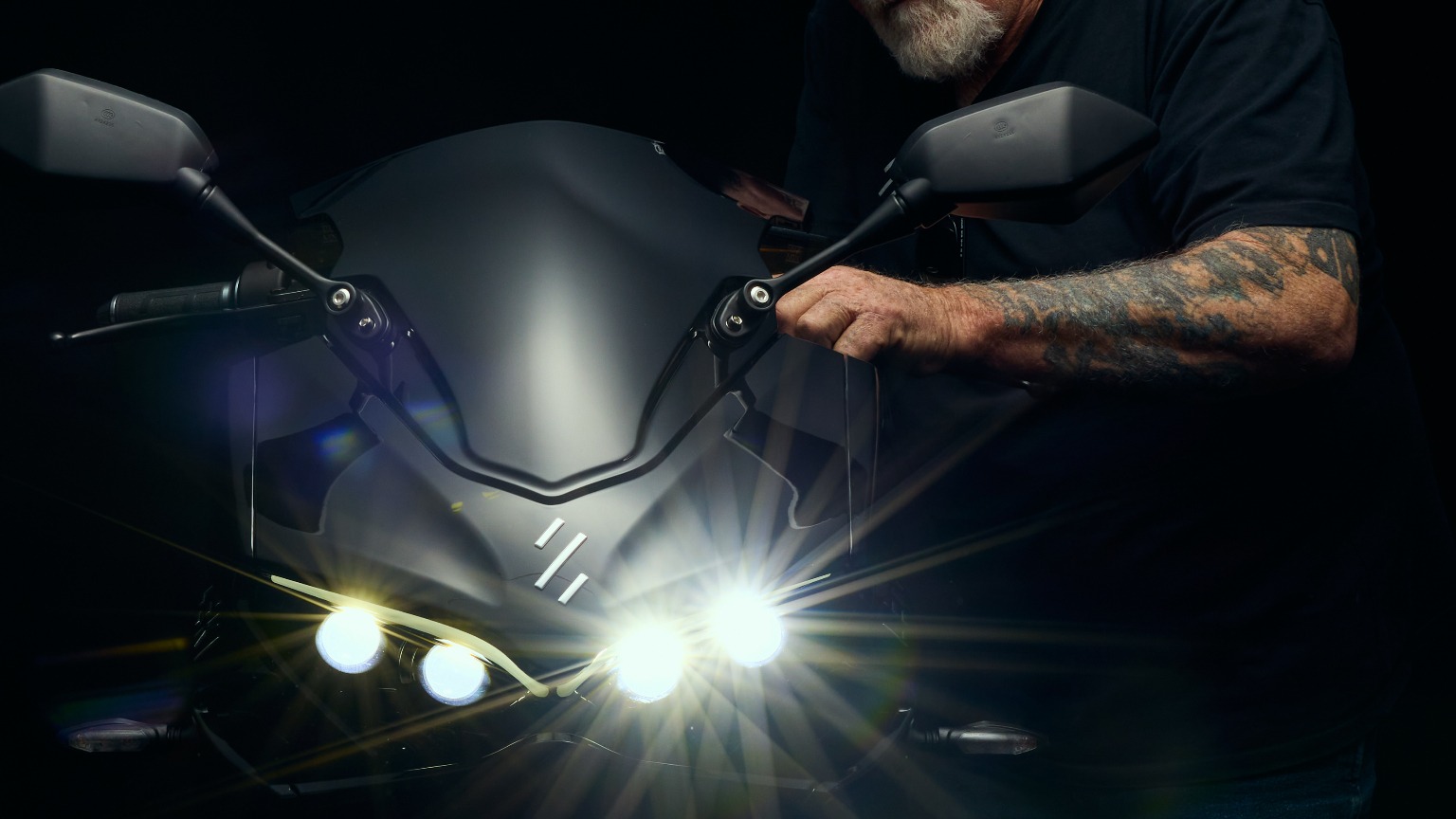Mechanic inspecting a LEKI E1 electric motorcycle with headlights lit